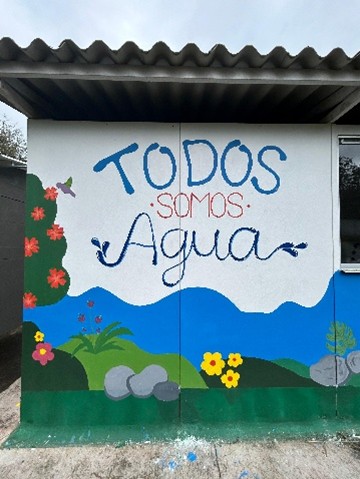 Photo 1. « Nous sommes tous de l’eau ». Peinture murale dans la zone de réserve paysanne de Venecia. Une image contenant ciel, écriture manuscrite, bâtiment, graffiti Le contenu généré par l’IA peut être incorrect.